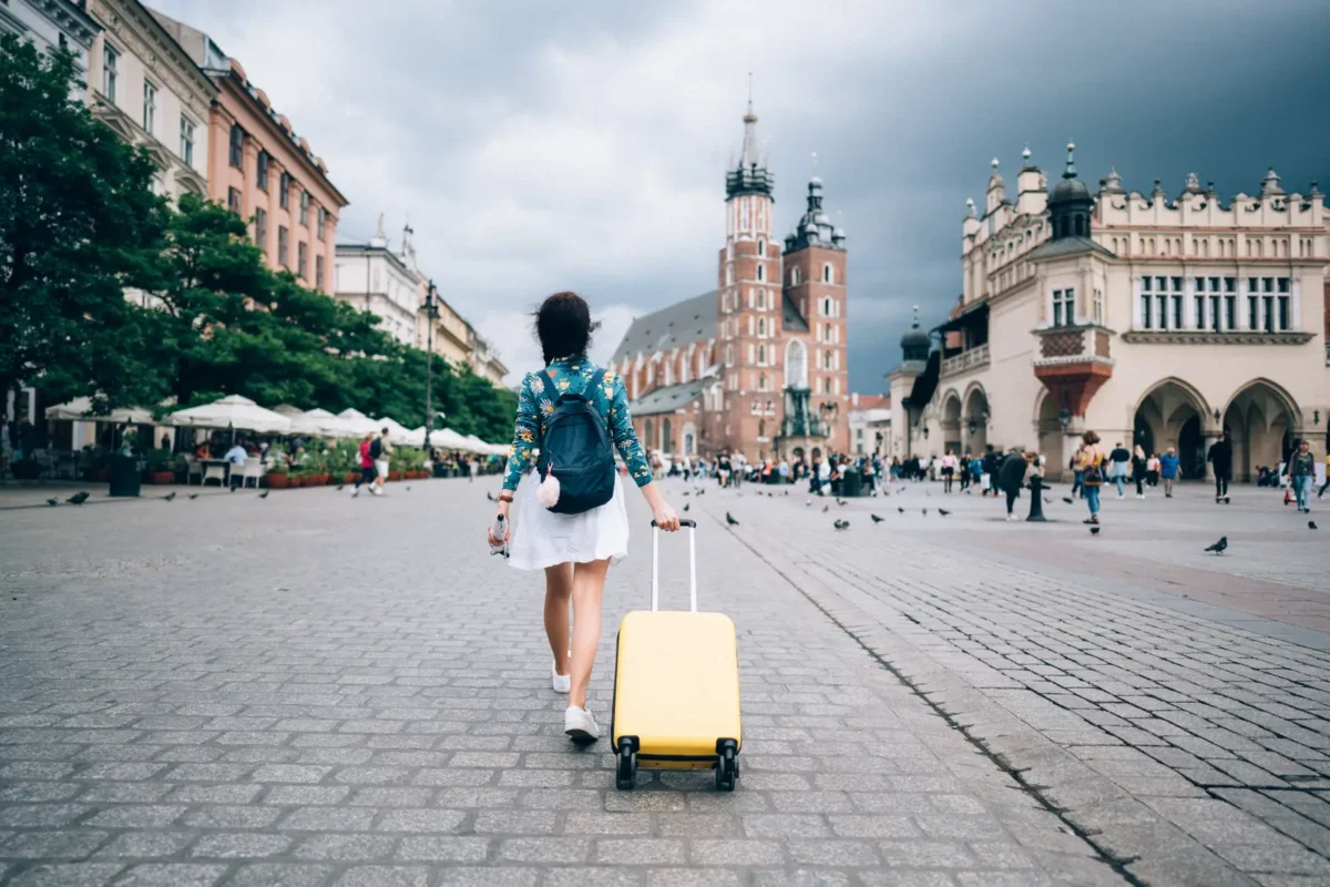 Femme voyageant seule avec une valise jaune sur une place historique en Europe, représentant l’aventure et la liberté du voyage en solo.